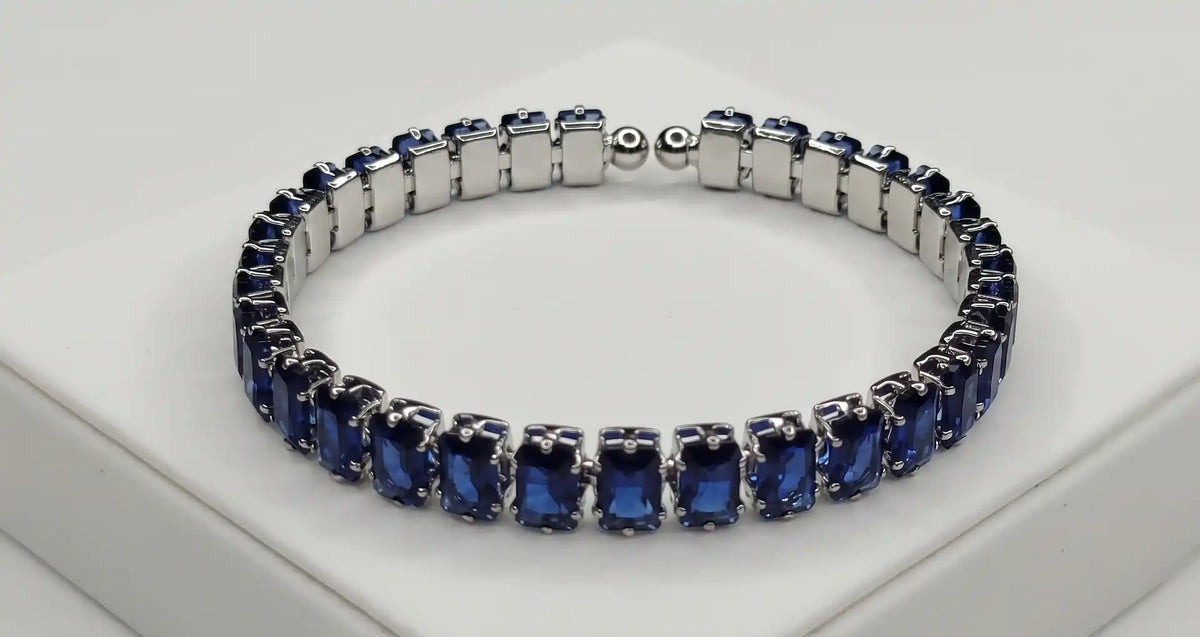 Deep blue emerald-cut sapphire tennis bracelet worn on a woman's wrist against a minimalist, neutral studio background.